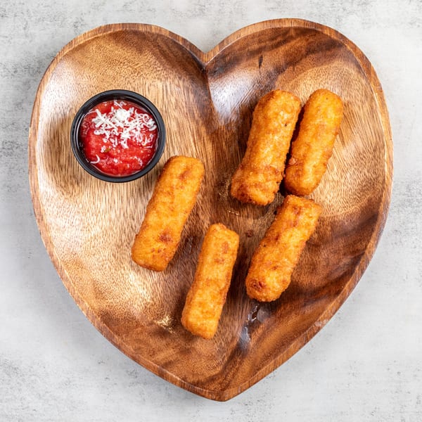 Five golden-brown mozzarella sticks and a cup of marinara sauce with grated cheese on a heart-shaped wooden plate.