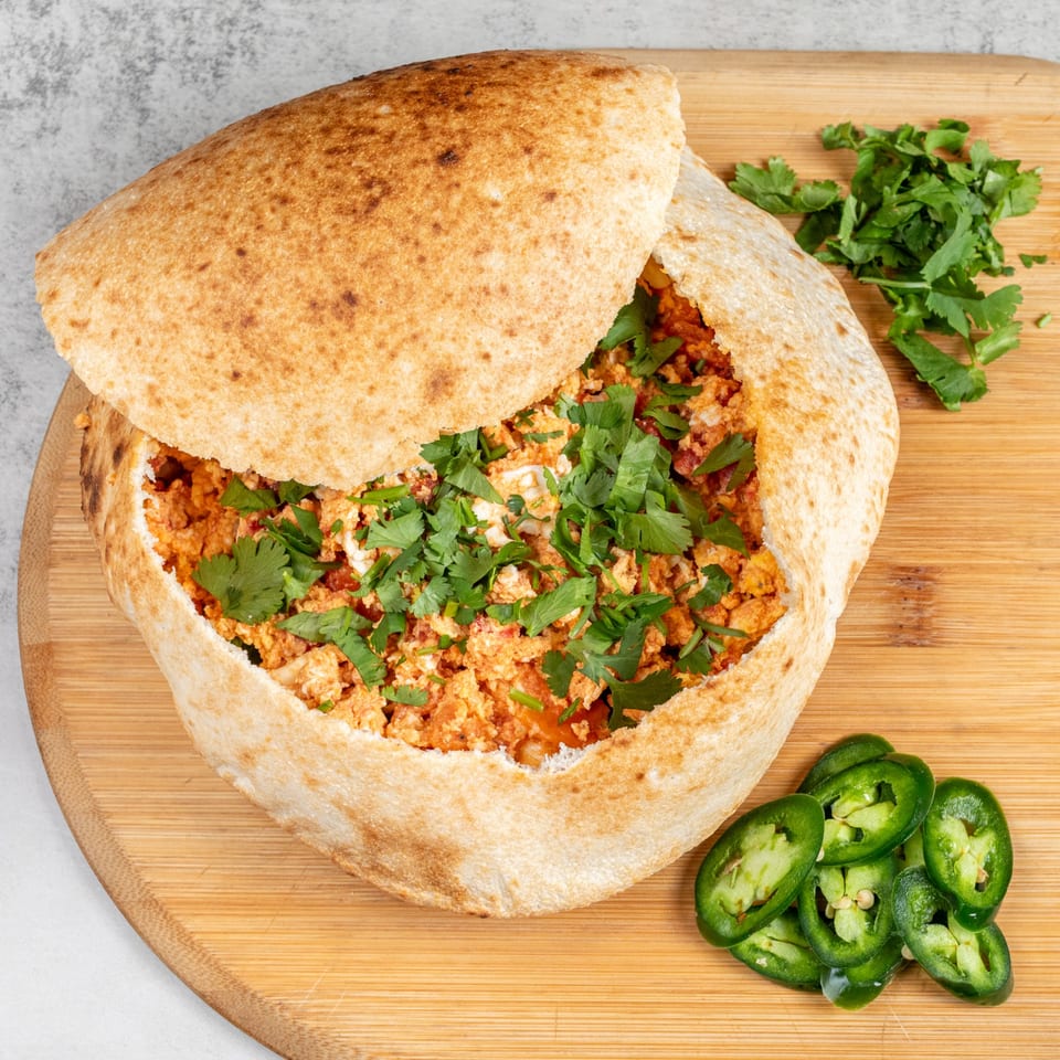 Baked pizza dough bowl filled with scrambled eggs, cheese, and cilantro, with jalapeños on the side.