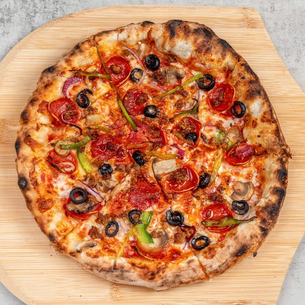 Baked Pizza's whole pepperoni, olive, mushroom, and pepper pizza on a wooden peel.