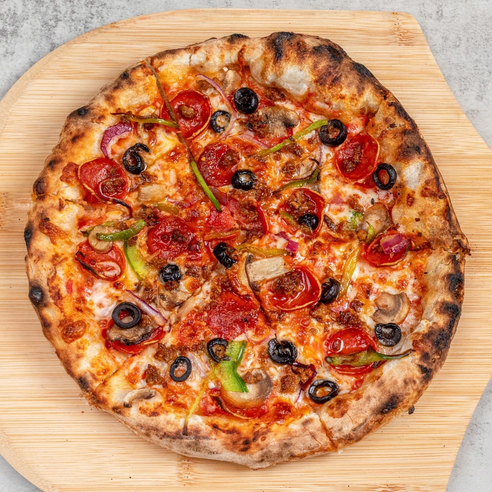 Baked Pizza's whole pepperoni, olive, mushroom, and pepper pizza on a wooden peel.
