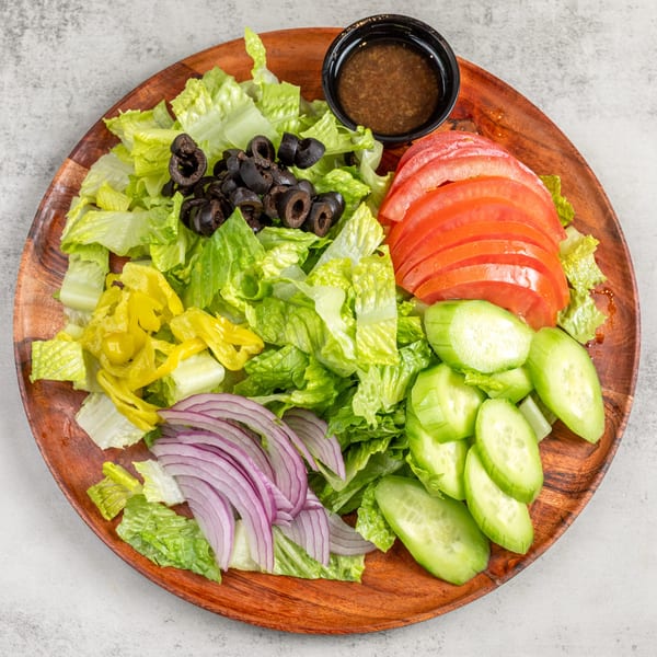A fresh garden salad with lettuce, tomatoes, cucumbers, olives, red onions, and dressing on a wooden plate.