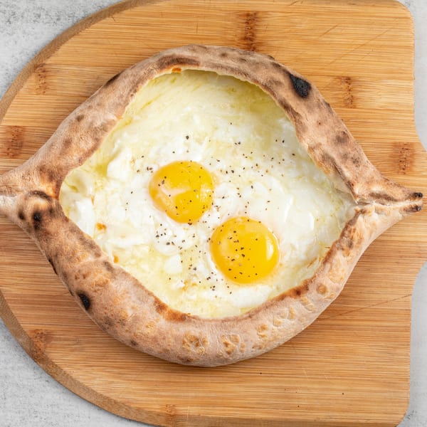 Baked Pizza and Sandwiches' boat-shaped pizza with melted cheese, two sunny-side-up eggs, and pepper.