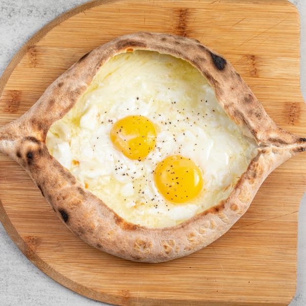 Baked Pizza and Sandwiches' boat-shaped pizza with melted cheese, two egg yolks, and black pepper.