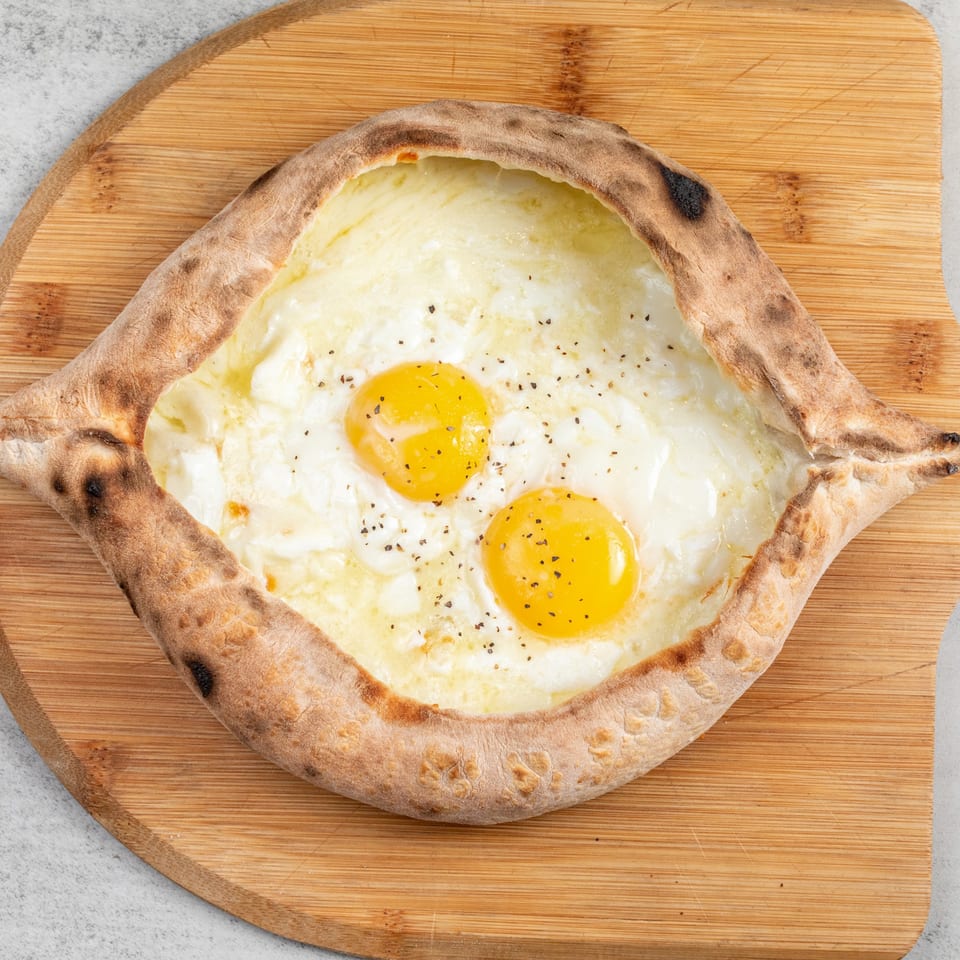 Baked Pizza and Sandwiches' boat-shaped pizza with melted cheese, two egg yolks, and black pepper.