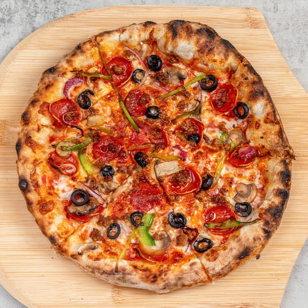 A freshly baked pizza with pepperoni, olives, mushrooms, and peppers on a wooden pizza peel.