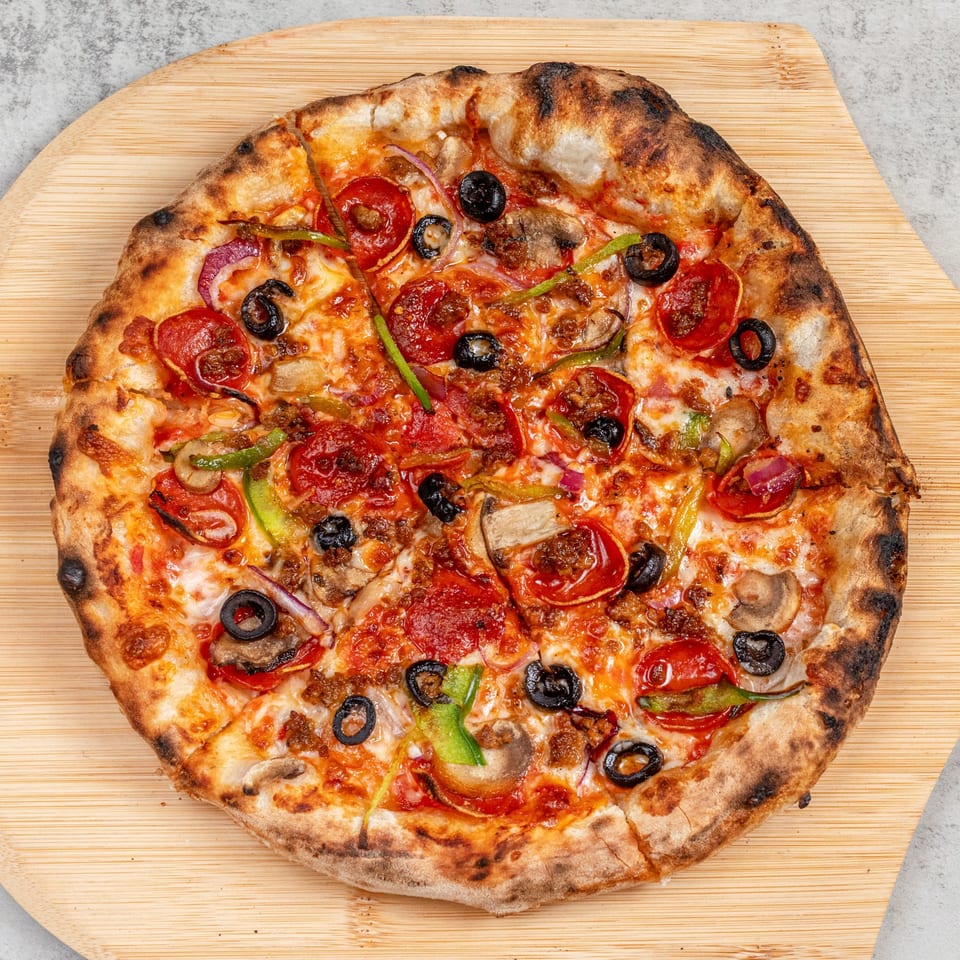A freshly baked pizza with pepperoni, olives, mushrooms, and peppers on a wooden pizza peel.