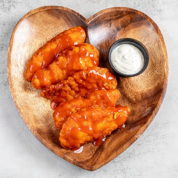 Buffalo chicken tenders with ranch dressing on a heart-shaped wooden plate.