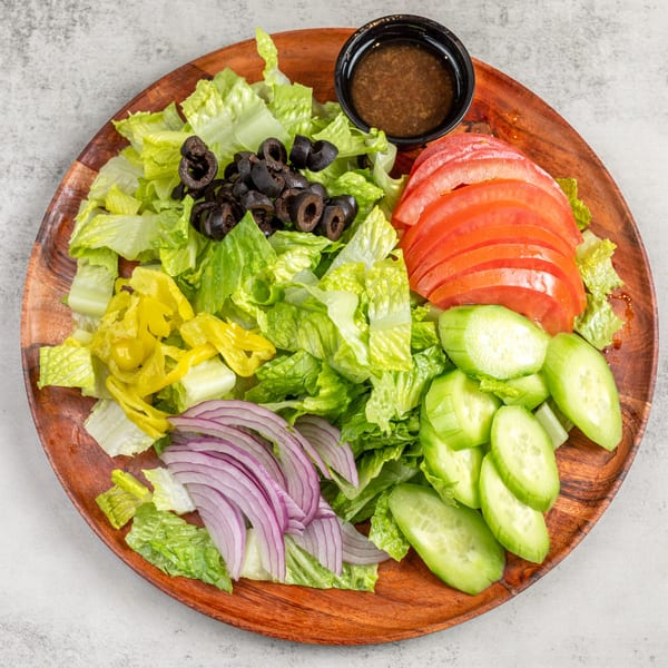 Fresh garden salad with lettuce, tomatoes, cucumbers, red onions, black olives, and pepperoncini on a wooden plate.
