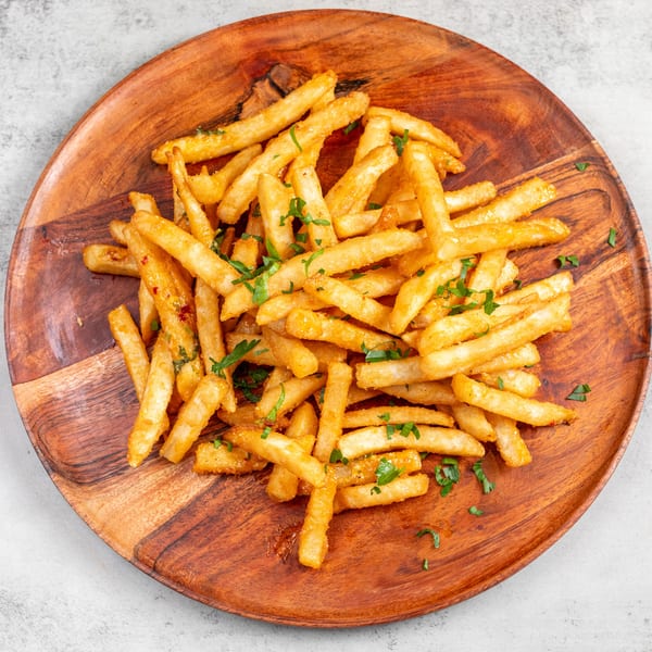Golden french fries, lightly seasoned with herbs, served on a rustic wooden plate.