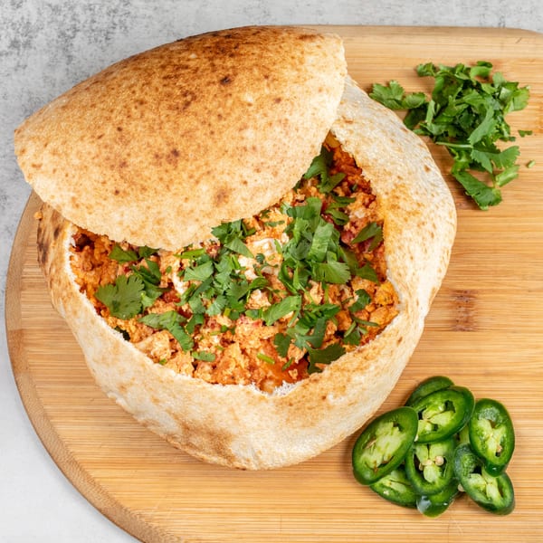 Baked pizza sandwich filled with chicken and cilantro, served with sliced jalapeños on a wooden board.