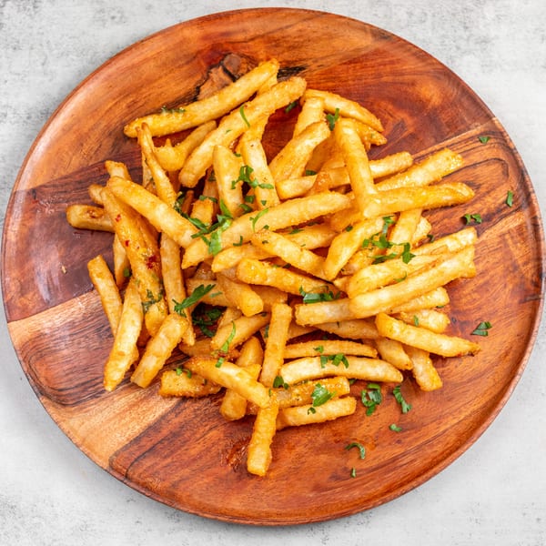 Golden brown french fries sprinkled with fresh parsley on a round wooden plate.