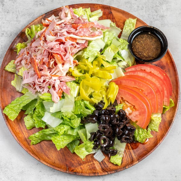 Antipasto salad with lettuce, deli meats, tomatoes, olives, and peppers on a wooden plate.